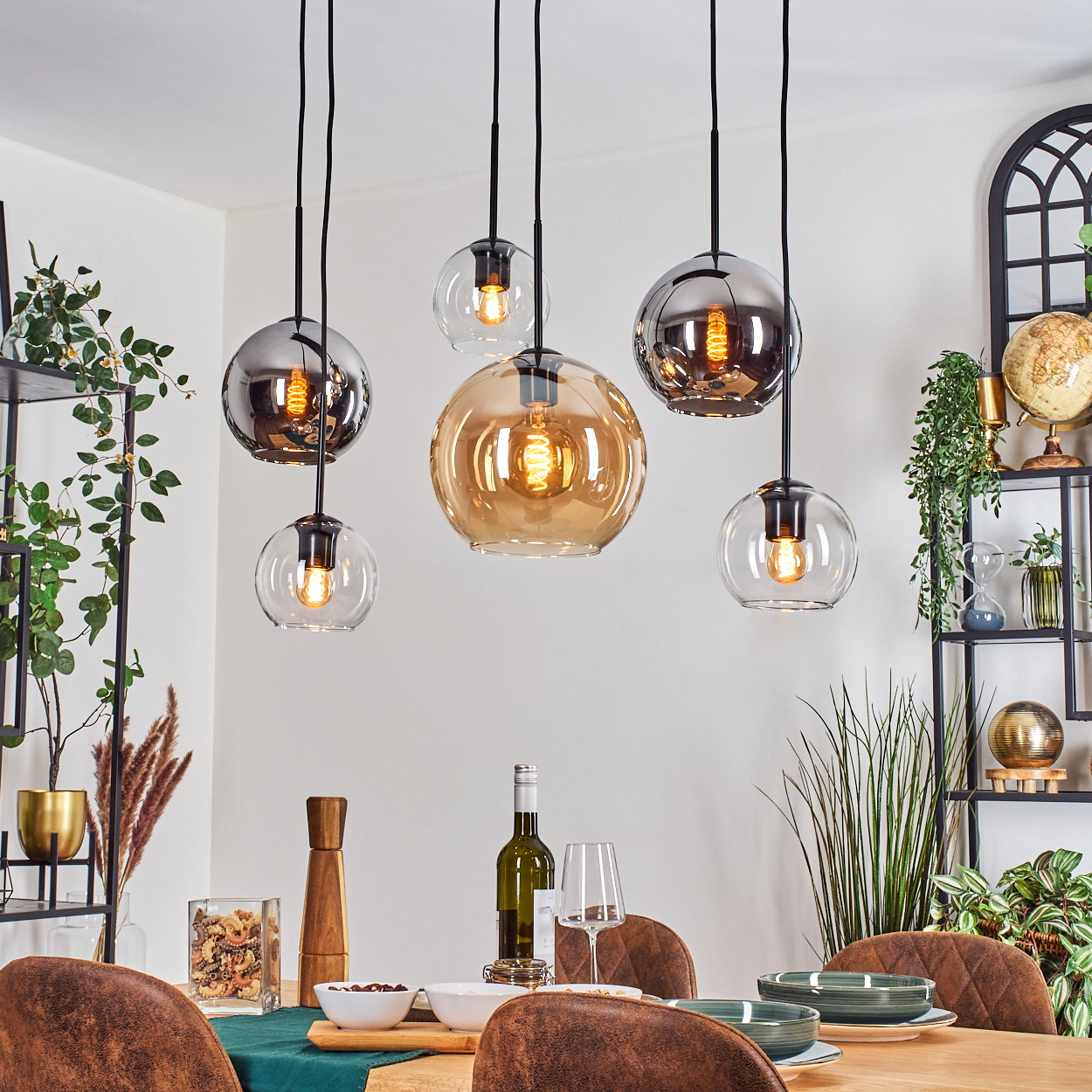 Esszimmer mit Hängelampen. Tisch für das Abendessen gedeckt. Pflanzen, Regale und ein Globus sind im Hintergrund.