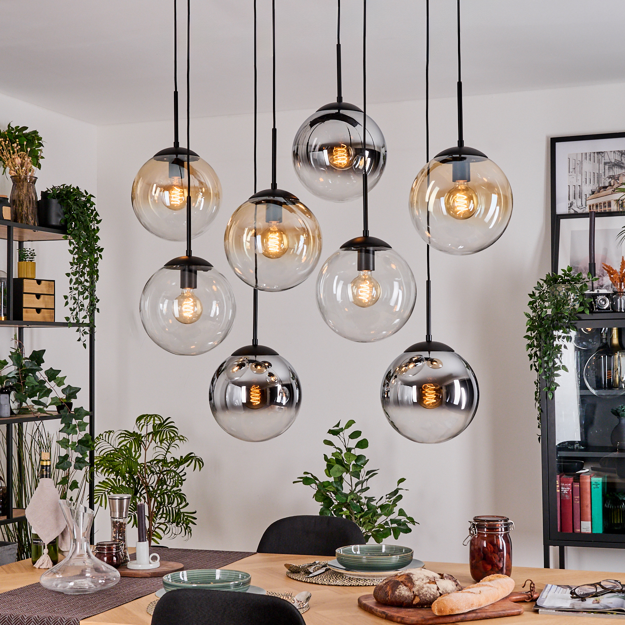 Esszimmer mit hängenden Kugelleuchten. Tisch mit Pflanzen und Essen gedeckt. Regale mit Dekorationen. Lichter spiegeln sich in den Kugeln.