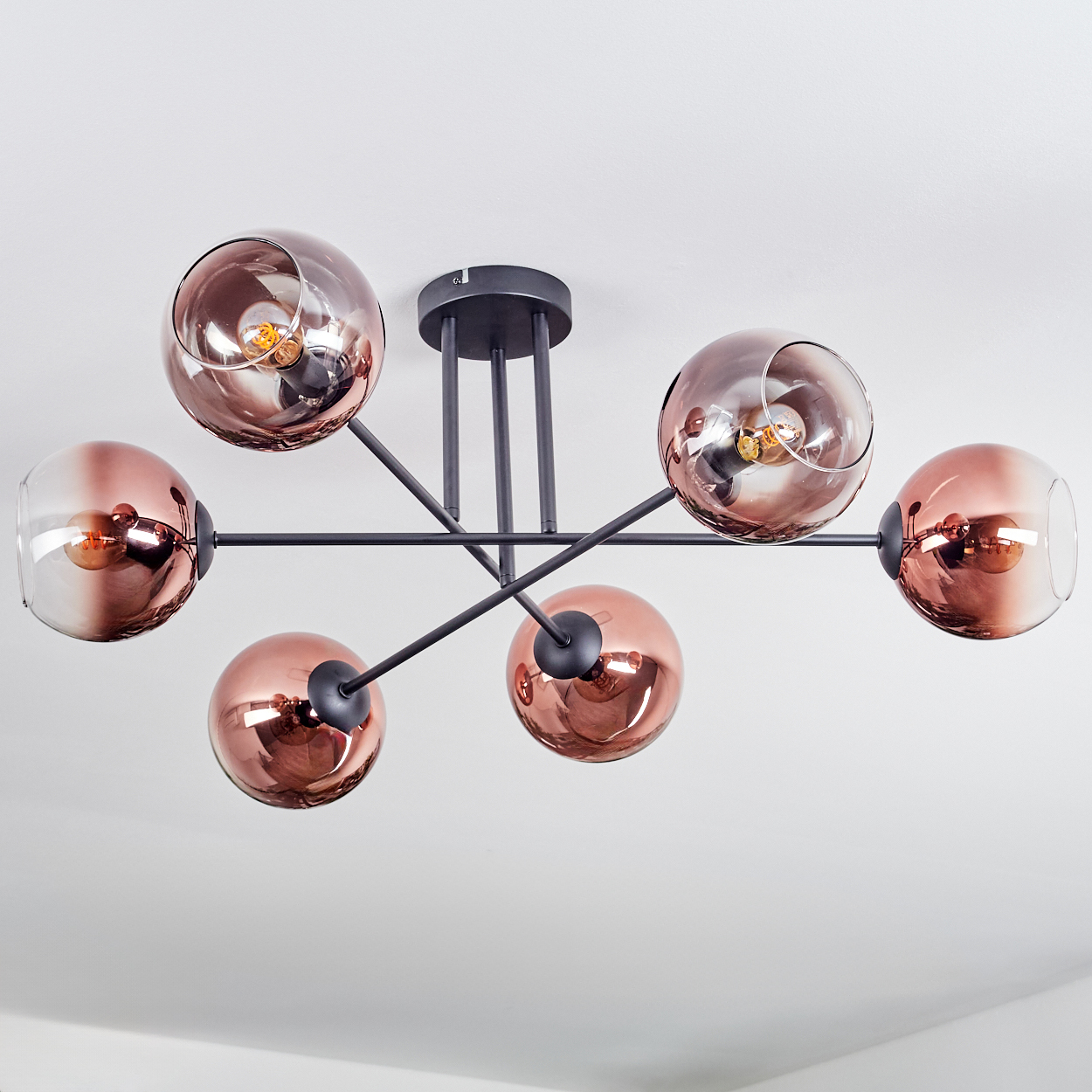 Eine moderne Deckenleuchte mit sechs kupferfarbenen Glaskugeln. Schwarze Metallarme erstrecken sich von einer zentralen Halterung.
