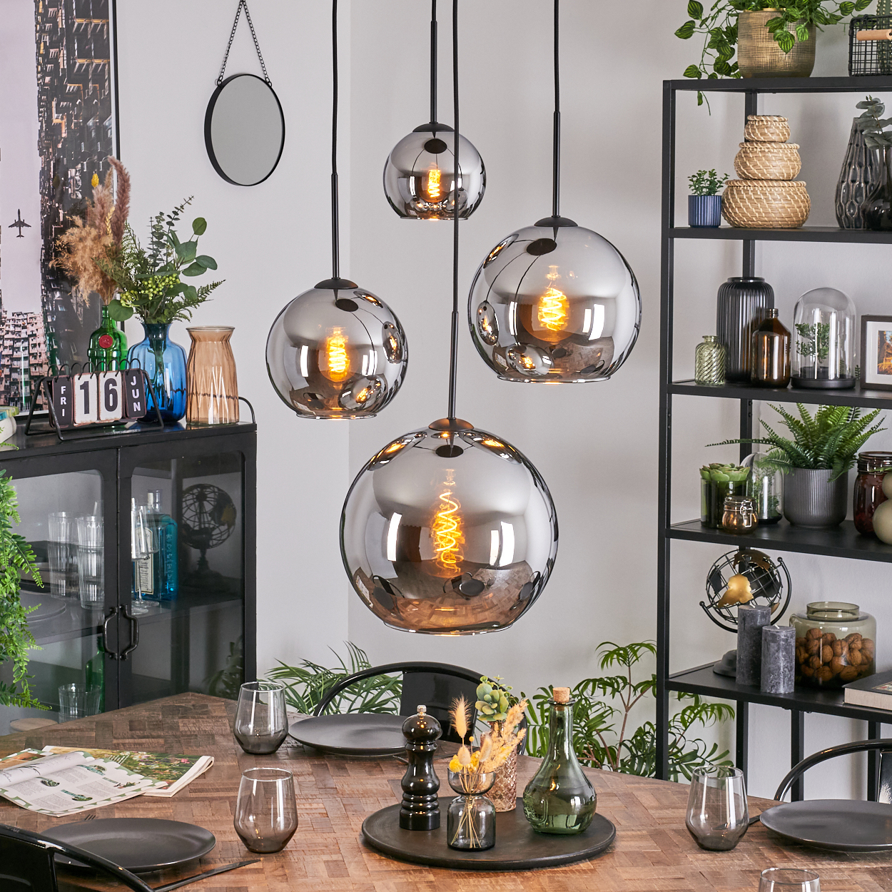 Esszimmer mit hängenden Kugellampen. Tisch mit Gläsern und Tellern gedeckt. Regale mit Pflanzen und Deko.