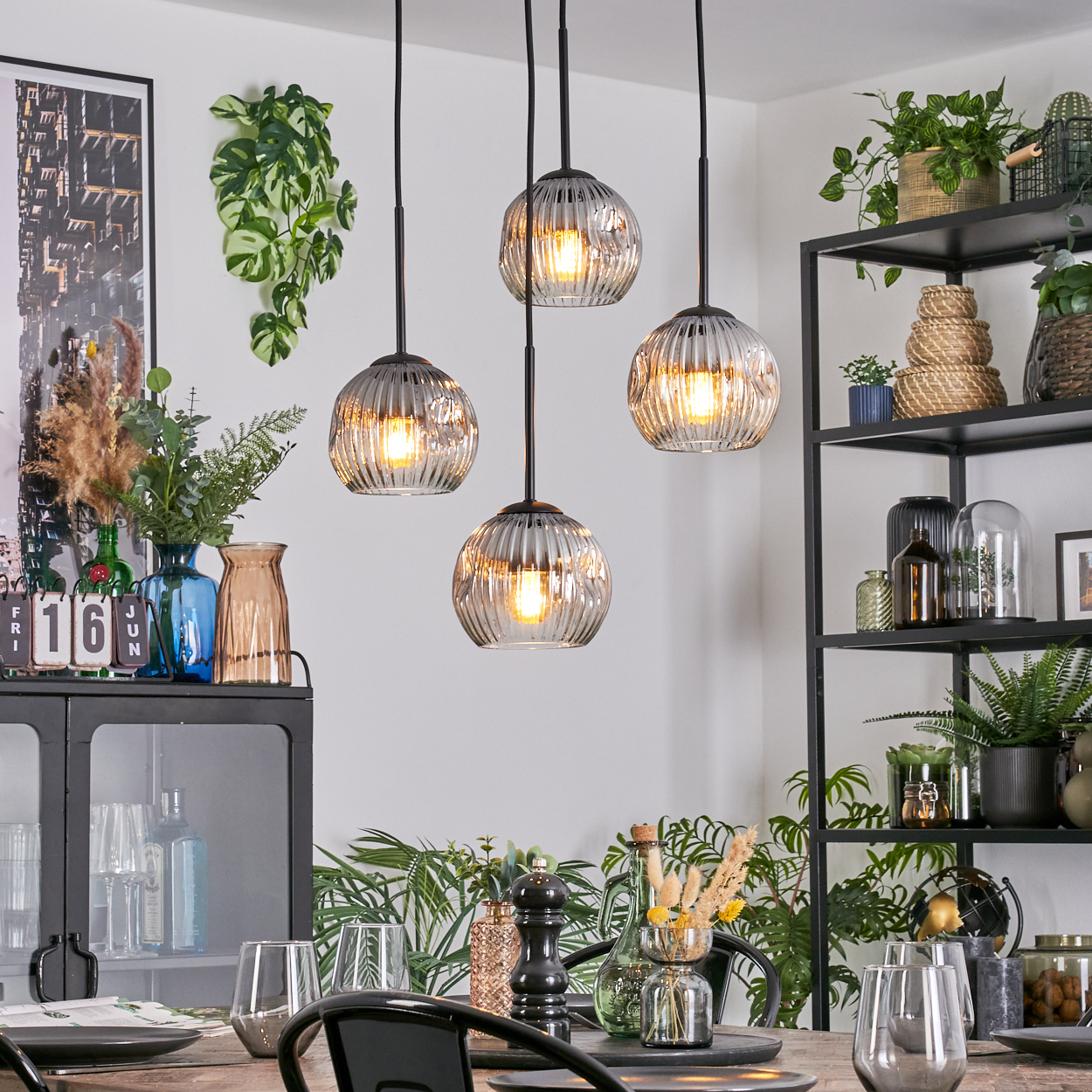 Esszimmer mit Hängelampen, Pflanzen und Regalen. Tisch mit Gläsern und Tellern. Hintergrund mit Dekoration und Grün.