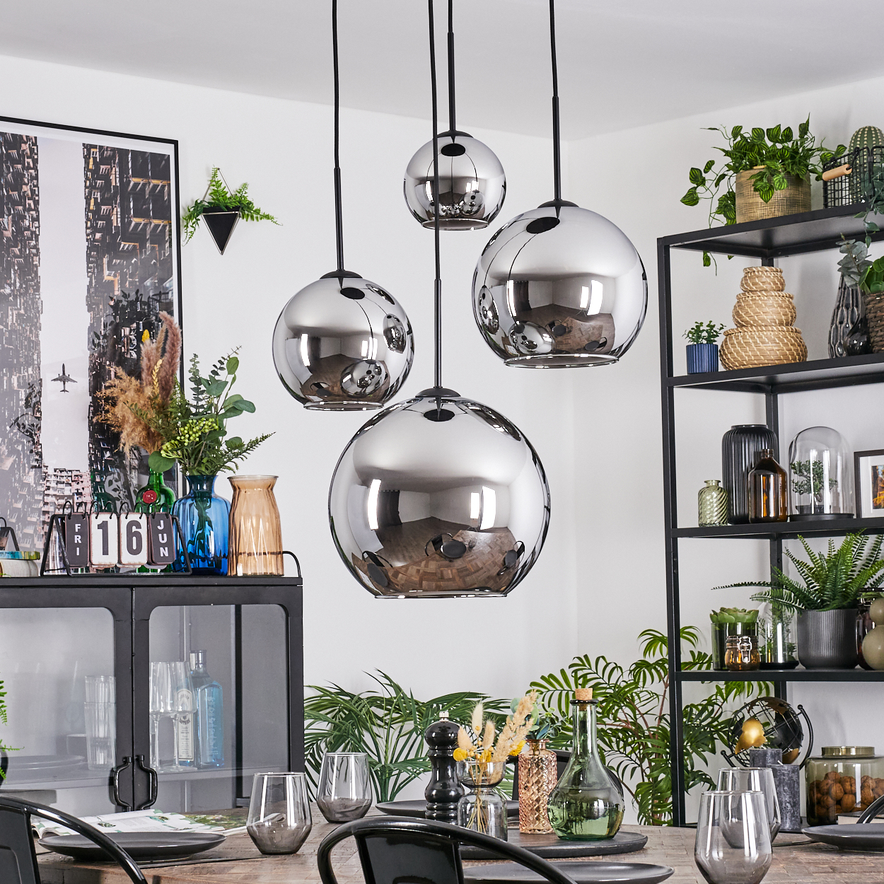 Esszimmer mit vier Chrom-Kugel-Pendelleuchten. Tisch mit Gläsern gedeckt. Pflanzen und Regale im Hintergrund.