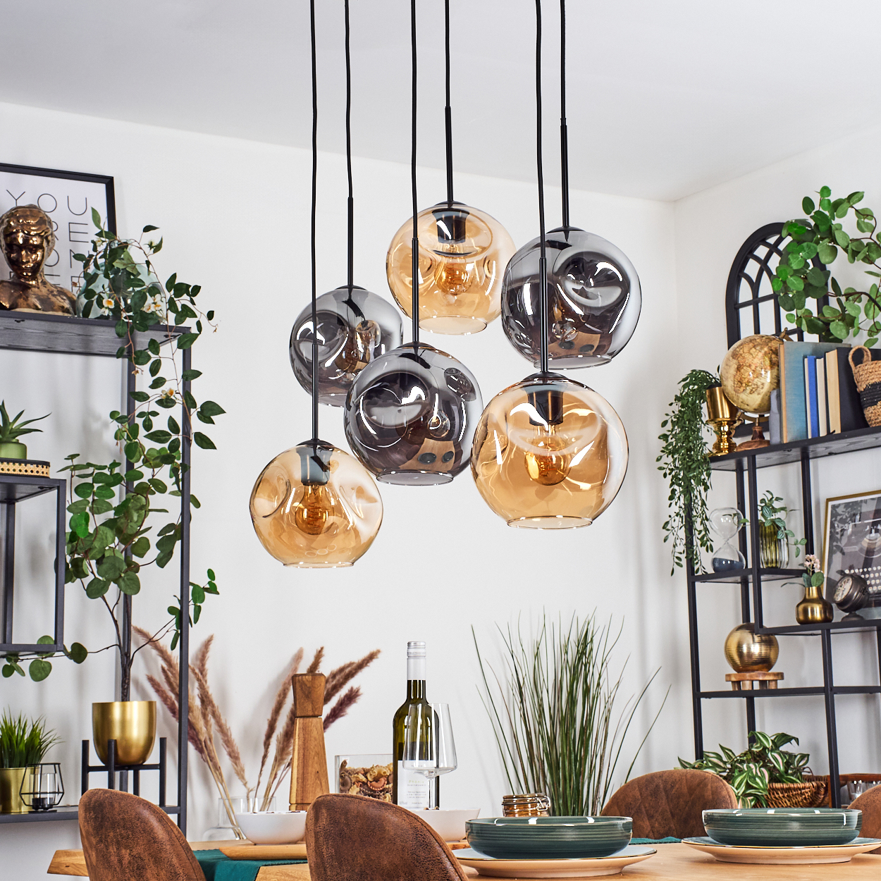 Esszimmer mit hängenden Kugelleuchten. Tisch mit Tellern, Wein und Stühlen. Regale mit Dekoration und Pflanzen im Hintergrund.