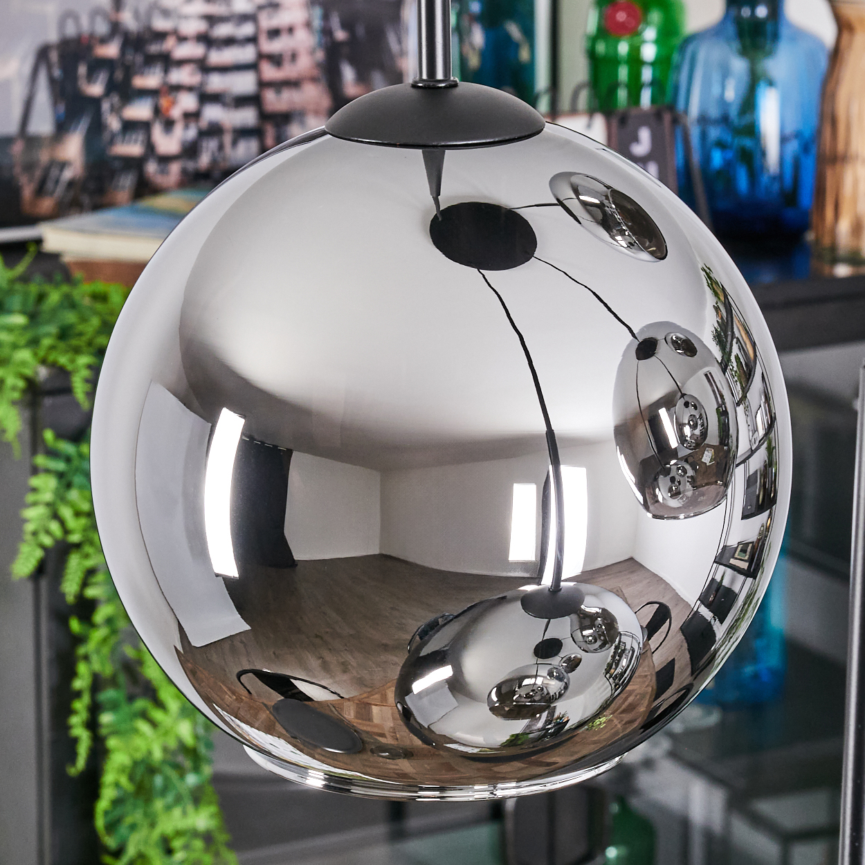 Eine reflektierende, kugelförmige Lampe hängt. Die Oberfläche der Lampe spiegelt einen Raum mit Holzböden und andere Objekte wider.