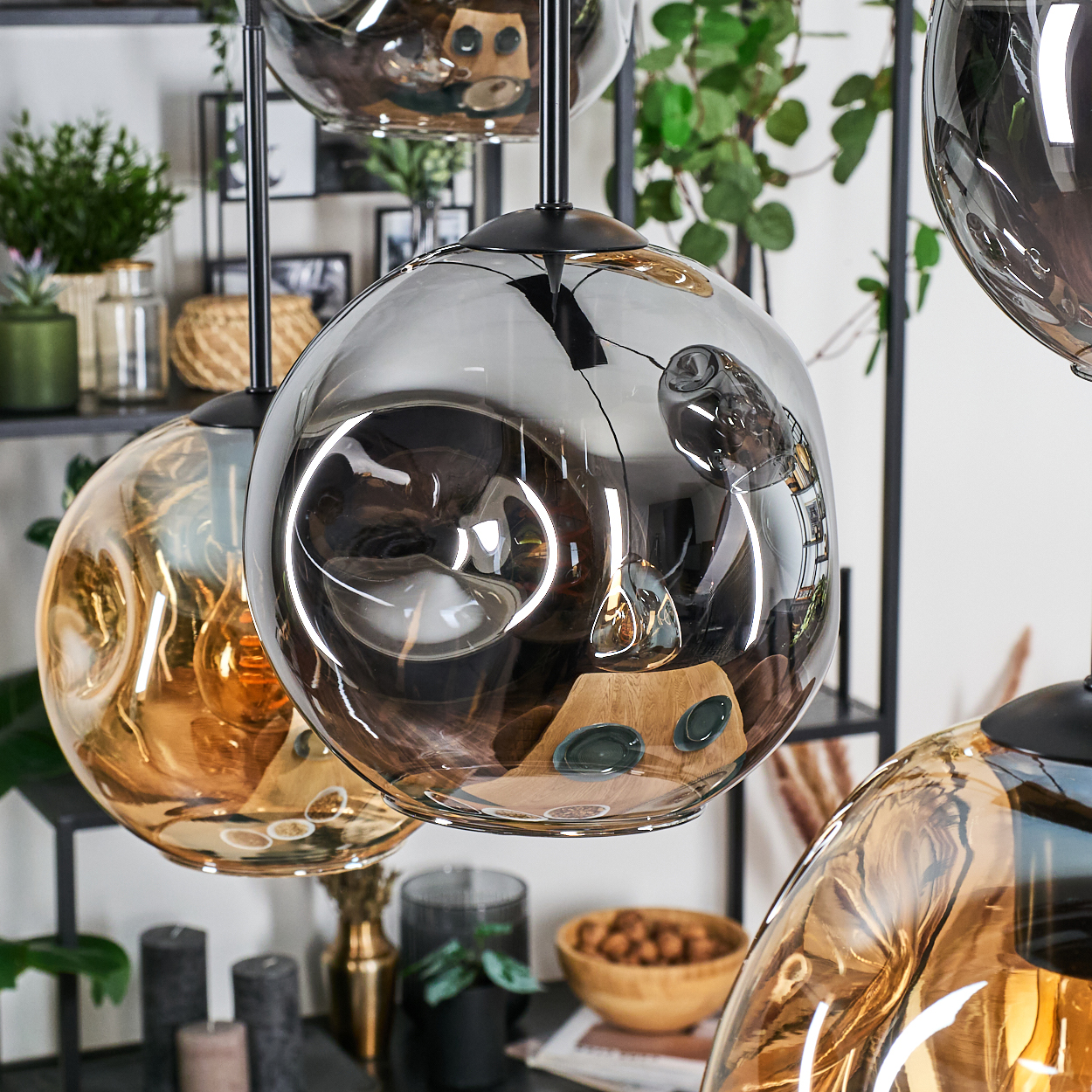Nahaufnahme von dekorativen Pendelleuchten. Die Glaskugeln reflektieren Objekte. Hintergrund zeigt Pflanzen, Kerzen und Dekoration.