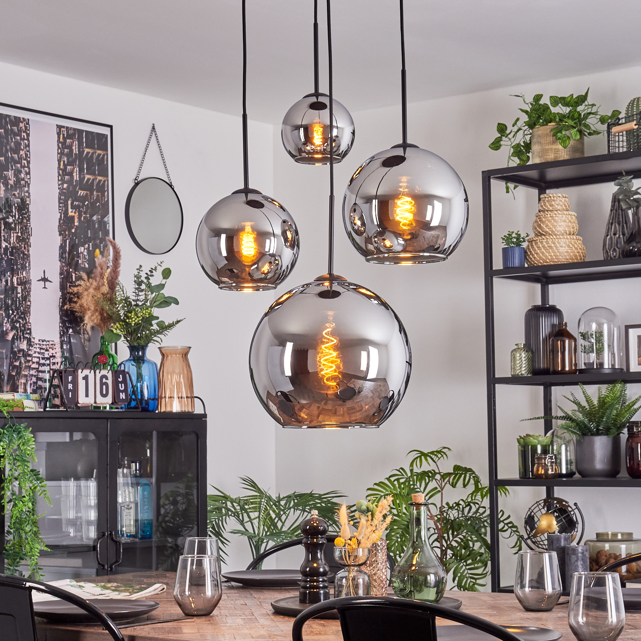 Esszimmer mit vier kugelförmigen Pendelleuchten. Ein Tisch ist mit Gläsern und Tellern gedeckt. Regale und Pflanzen sind im Hintergrund.