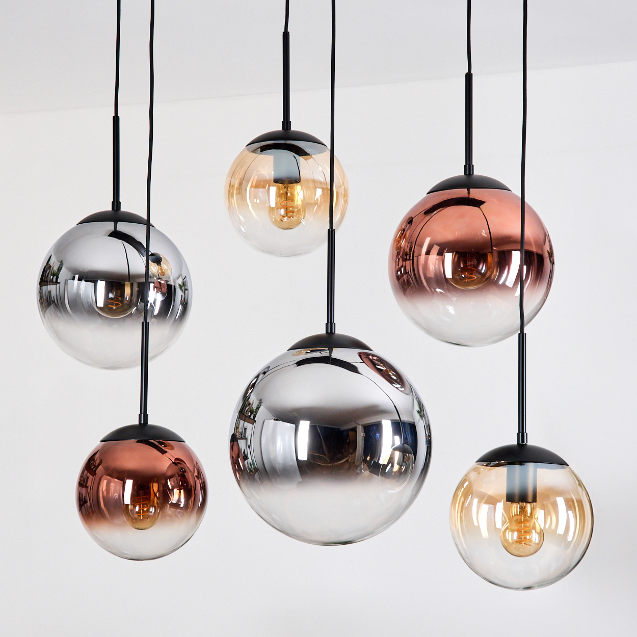 Sechs moderne Pendelleuchten mit kugelförmigen Glasschirmen in Silber-, Kupfer- und Bernsteintönen hängen vor weißem Hintergrund.