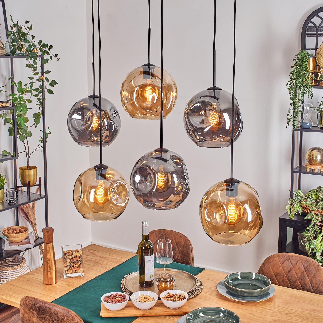 Esszimmer mit hängenden Blasenlichtern. Tisch gedeckt mit Tellern, Snacks und Wein. Regale mit Pflanzen, Dekor und braunen Lederstühlen.