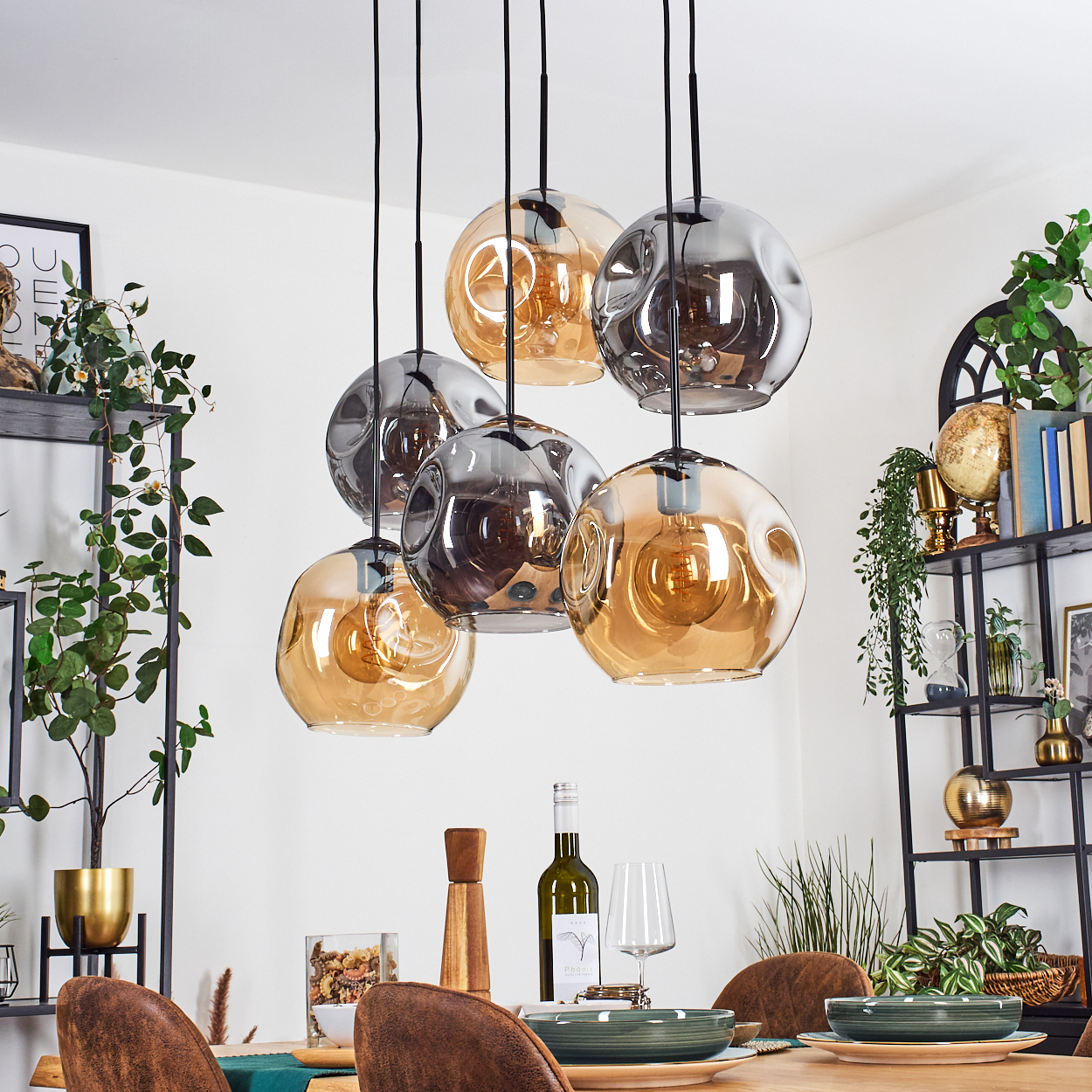 Esszimmer mit hängenden Kugelleuchten. Tisch mit Tellern, Gläsern und einer Weinflasche. Regale mit Dekor und Pflanzen.