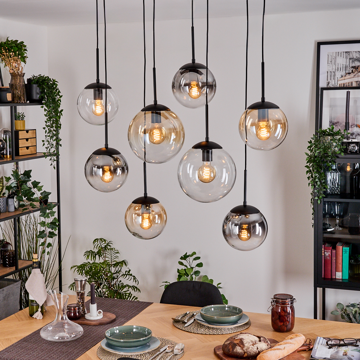 Ein Esszimmer mit Hängeleuchten. Ein Tisch ist mit Tellern, Brot und einem Glas Essen gedeckt. Regale beherbergen Pflanzen und Dekoration.