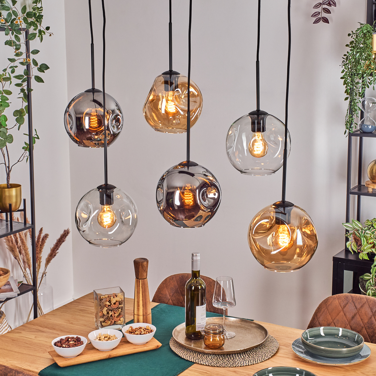 Esszimmer mit Hänge-Glühbirnen, Holztisch für das Abendessen mit Wein und Essen und Pflanzen im Hintergrund.