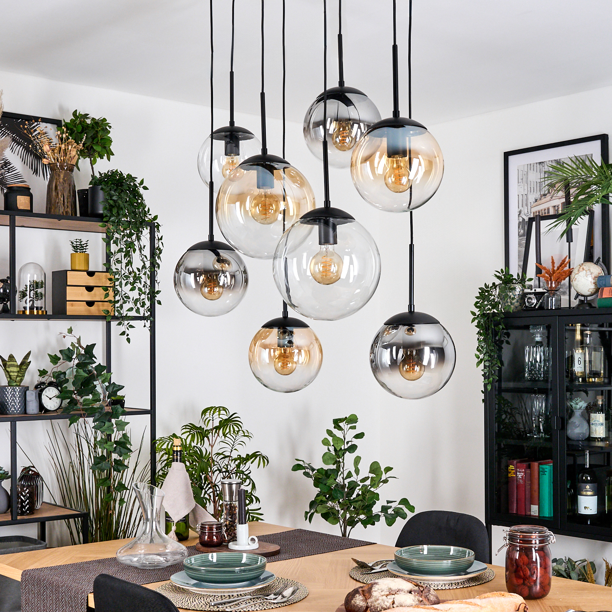 Esszimmer mit Holztisch, Glaskugellampen, Pflanzen und schwarzem Schrank mit Büchern und Dekoration.