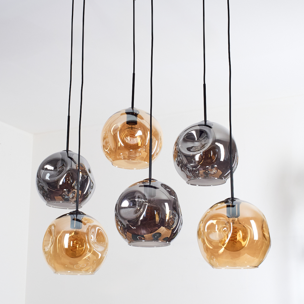 Sechs moderne Pendelleuchten mit strukturierten Glasschirmen. Einige sind bernsteinfarben, andere rauchgrau. Schwarze Kabel hängen von der Decke.