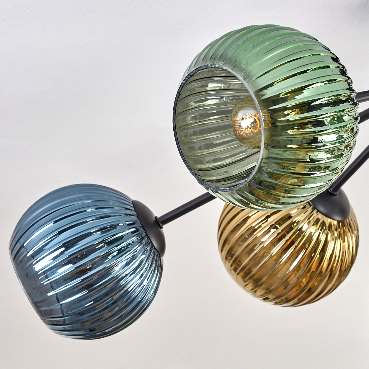 Eine moderne Deckenlampe mit drei Glaskugeln in Grün, Blau und Gold. Die Kugeln haben eine gerippte Textur und sind von innen beleuchtet.