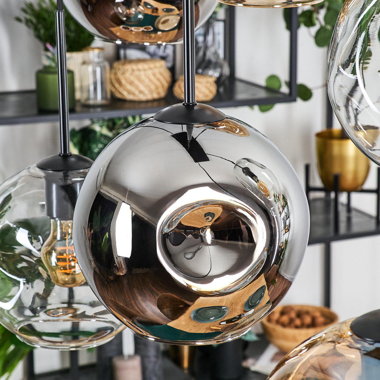 Hängende Pendelleuchten aus Chrom und Glas. Im Hintergrund sind Regale mit Dekoration zu sehen. Reflektierende Oberflächen und weiche Beleuchtung.