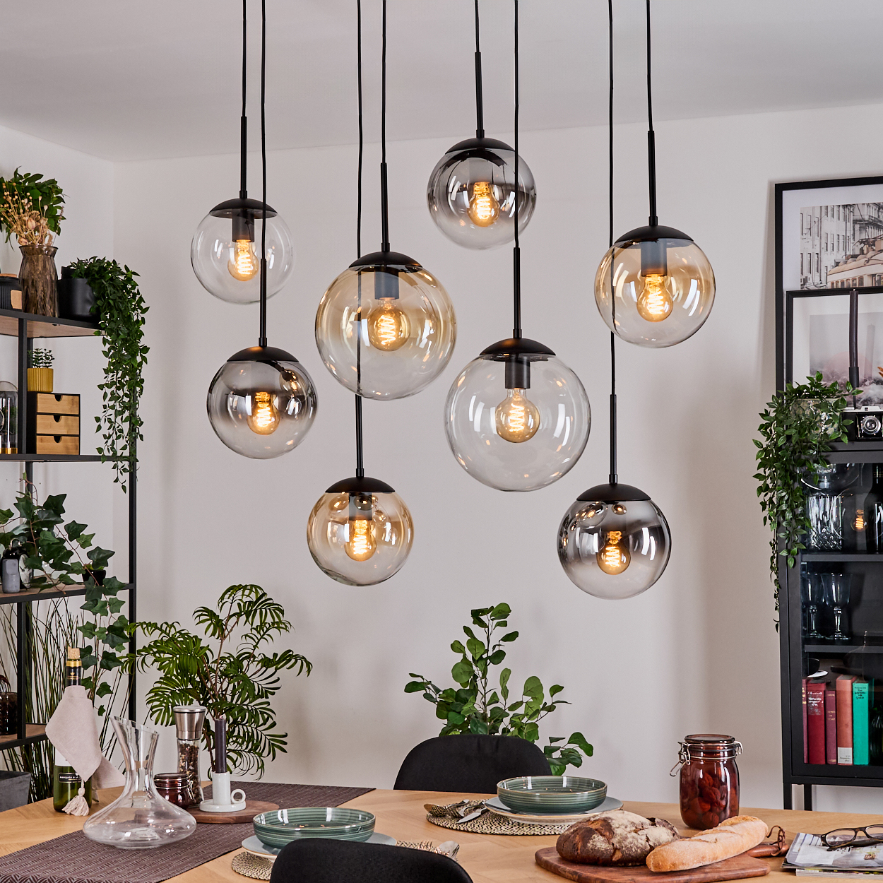Esszimmer mit acht kugelförmigen Hängelampen. Tisch mit Essen und Geschirr gedeckt. Regale mit Pflanzen und Dekoration.