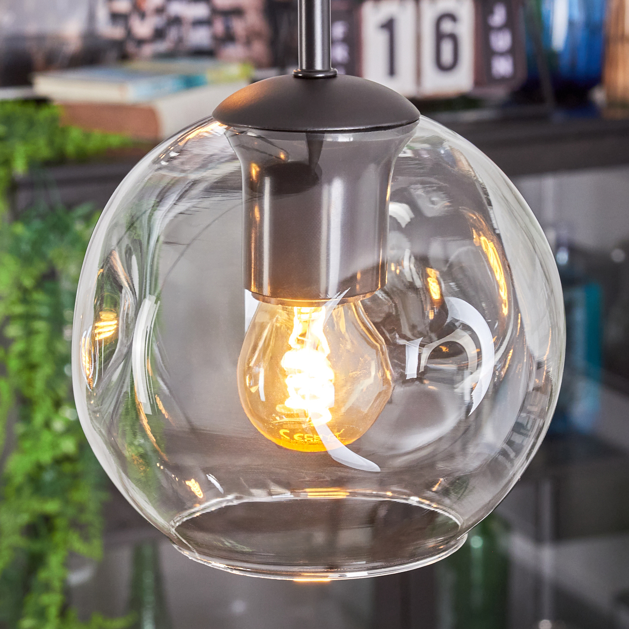 Eine klare Glaskugel-Hängeleuchte mit einer glühenden Glühbirne im Inneren. Die Leuchte ist aufgehängt, mit einer dunklen Metallfassung.