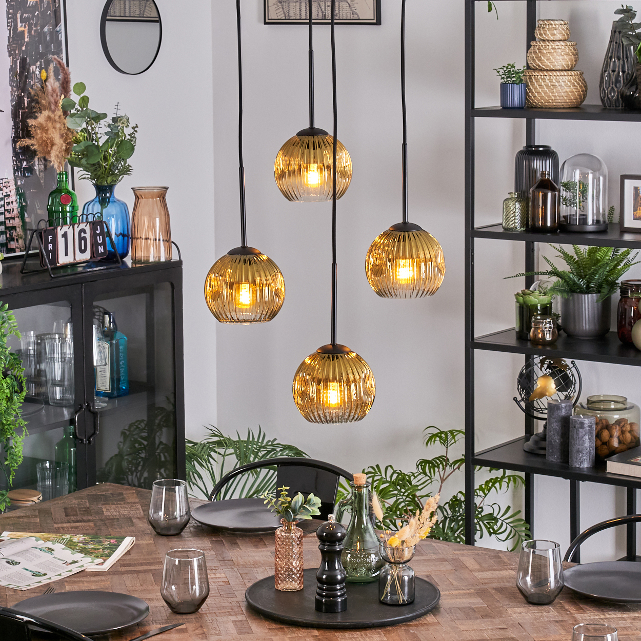 Esszimmer mit Holztisch, Gläsern, Tellern und Hängelampen mit goldenen Glasschirmen. Regale mit Dekoration.