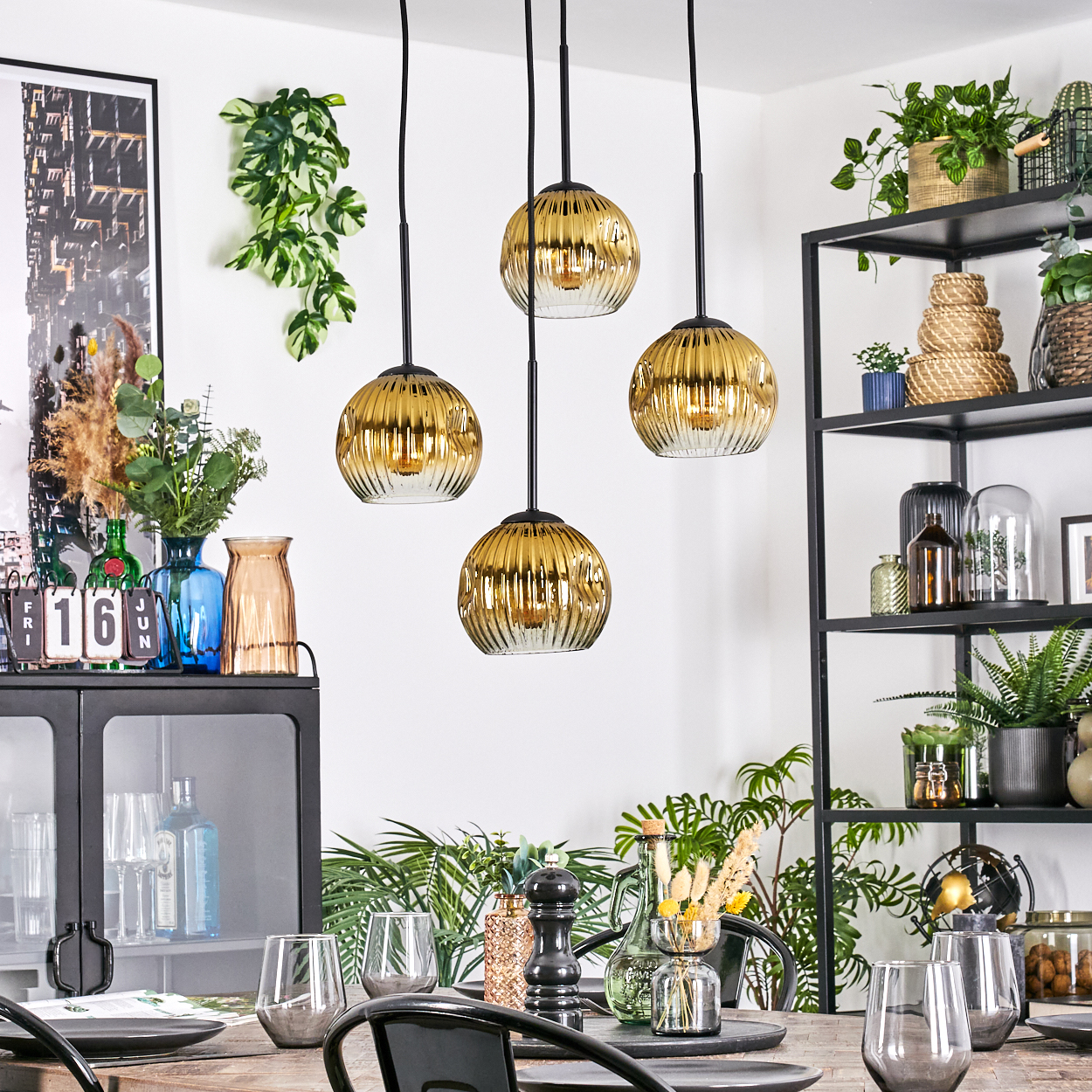 Esszimmer mit goldenen Hängelampen. Ein schwarzes Regal mit Pflanzen. Ein Tisch mit Gläsern und Dekorationen.