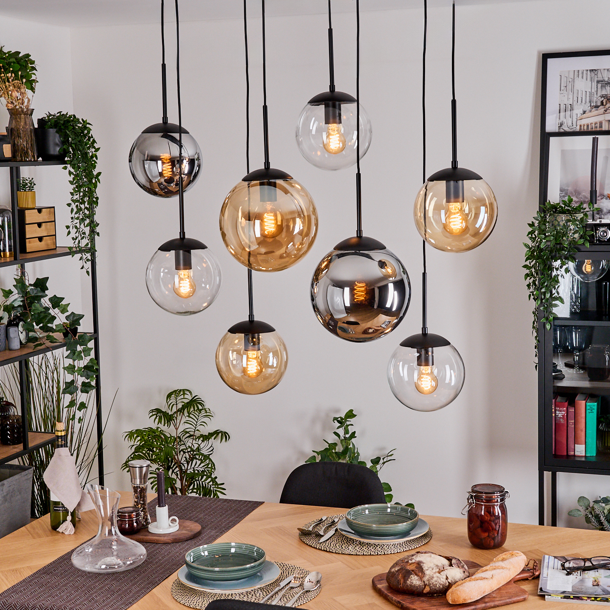 Esszimmer mit Holztisch, Hängeleuchten und Pflanzen. Tisch gedeckt mit Tellern, Brot und einem Glas mit Lebensmitteln.