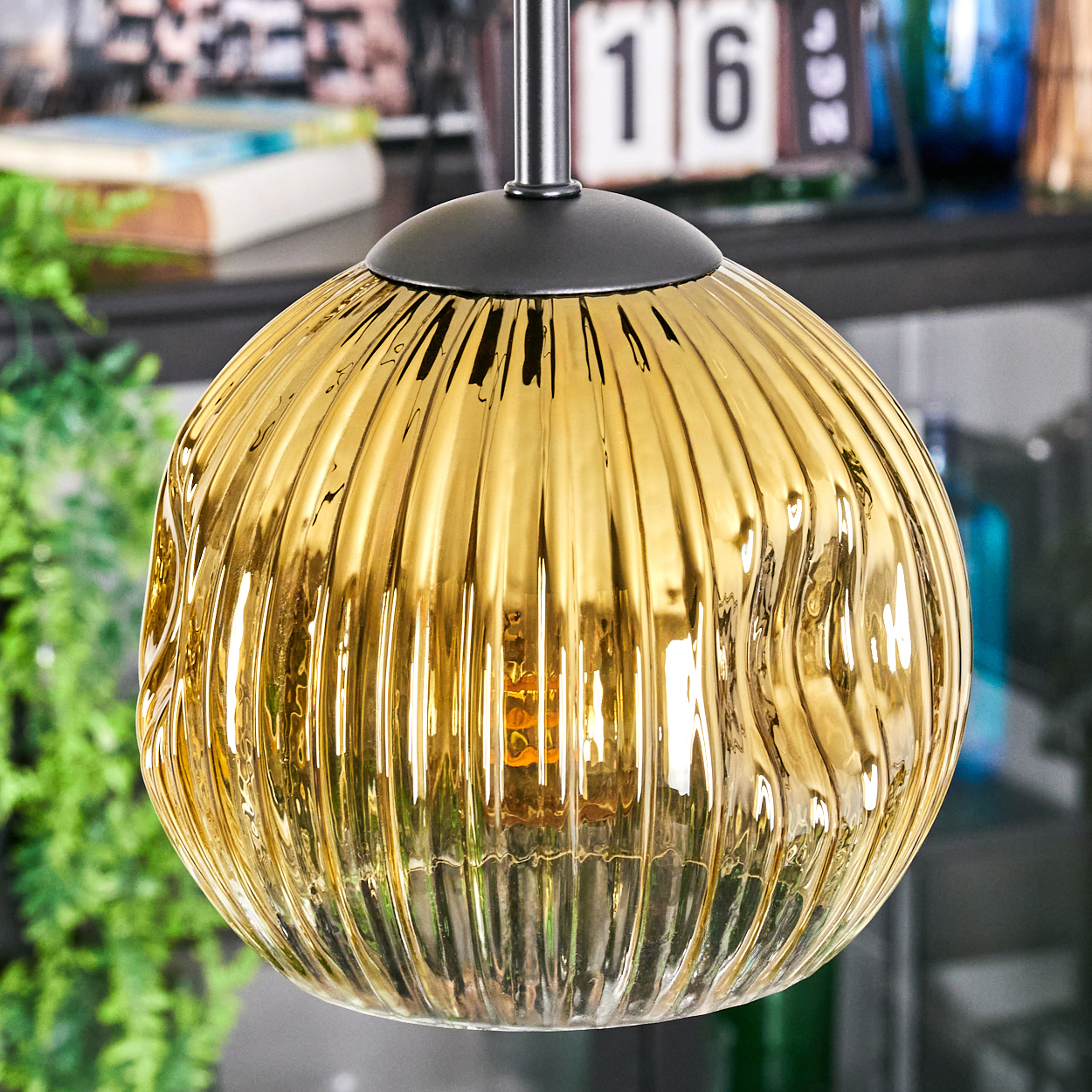 Eine goldene, gerippte Glas-Pendelleuchte hängt. Dahinter zeigt ein Kalender die '16', und Grün ist sichtbar.