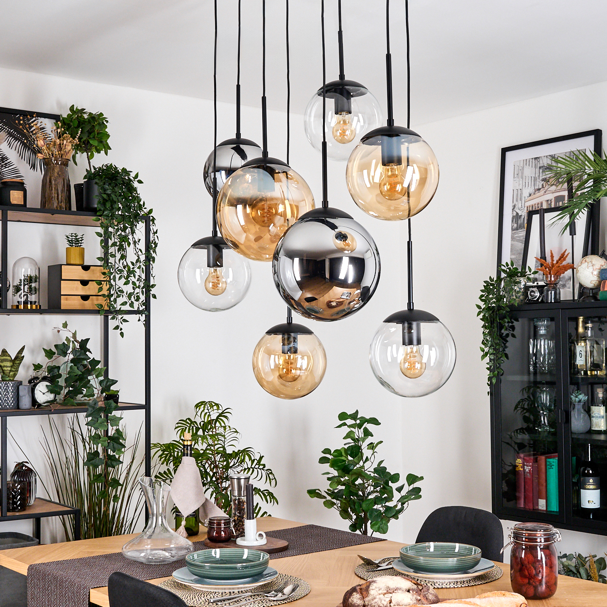 Ein Esszimmer mit Hängeleuchten, einem gedeckten Tisch, Pflanzen, Regalen mit Dekor und einem Glasschrank.