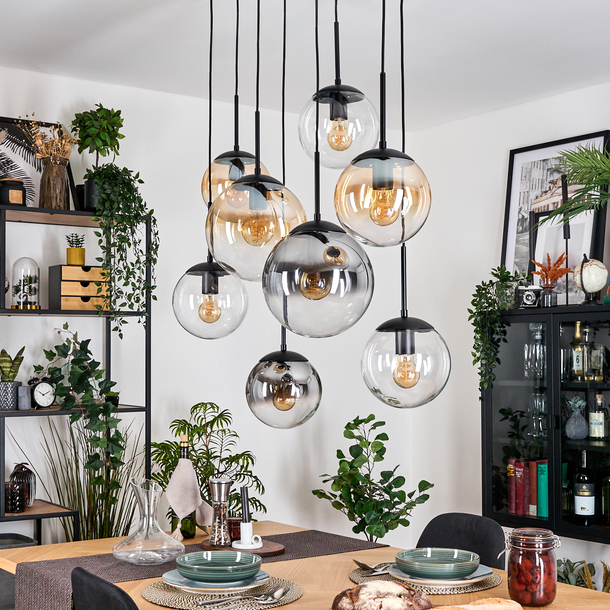 Ein Esszimmer mit Holztisch, Hängelampen. Pflanzen, ein schwarzer Schrank und ein gedeckter Tisch.