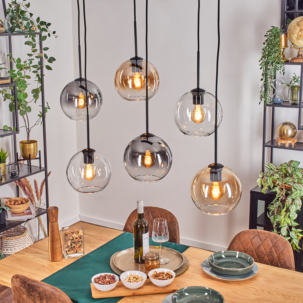 Esszimmer mit hängenden Kugelleuchten. Tisch mit Essen, Wein und Tellern. Regale mit Pflanzen und Dekor im Hintergrund.
