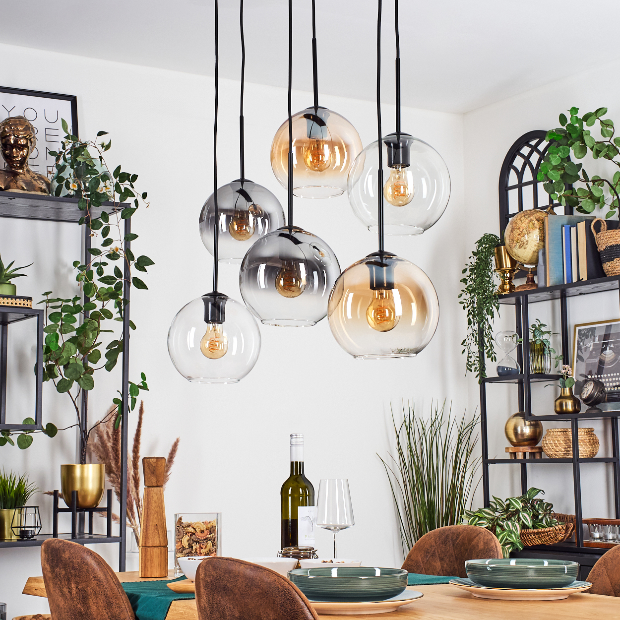 Esszimmer mit hängenden Kugelleuchten. Tisch mit Tellern, Weingläsern gedeckt. Regale mit Pflanzen und Dekoration sind sichtbar.