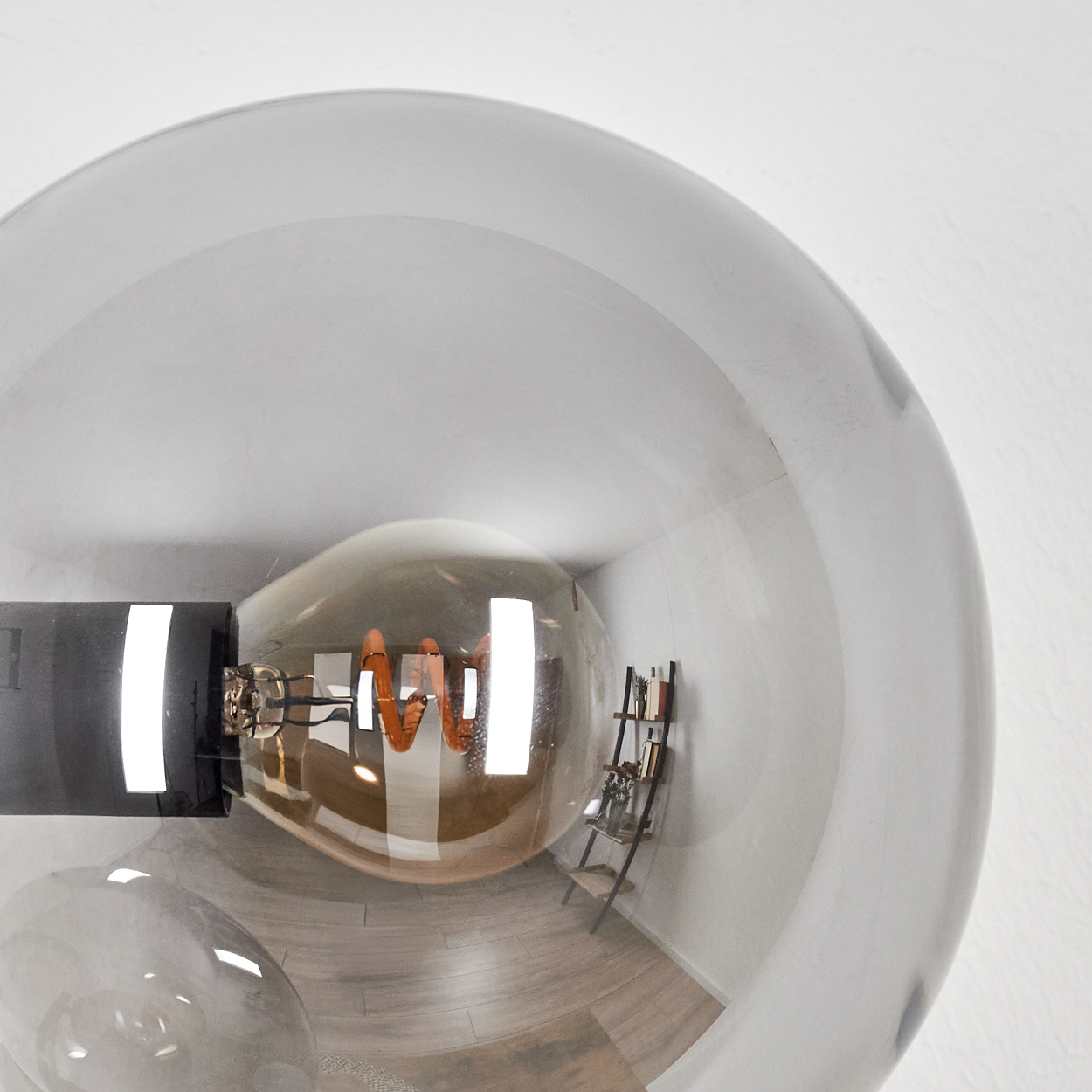Nahaufnahme einer Glühbirne in einer Glaskugel. Im Hintergrund ist ein kleines Regal mit Büchern und Gegenständen zu sehen.