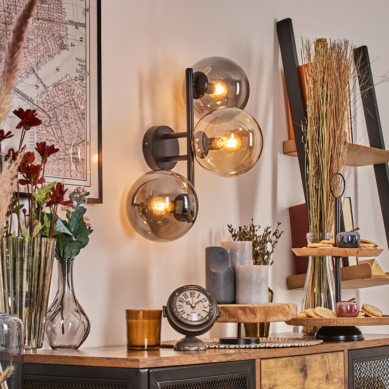 Ein Raum mit Lampe, Karte, Blumen, Uhr und Regalen. Die Lampe hat drei Glaskugeln. Verschiedene Dekorationsartikel sind ausgestellt.