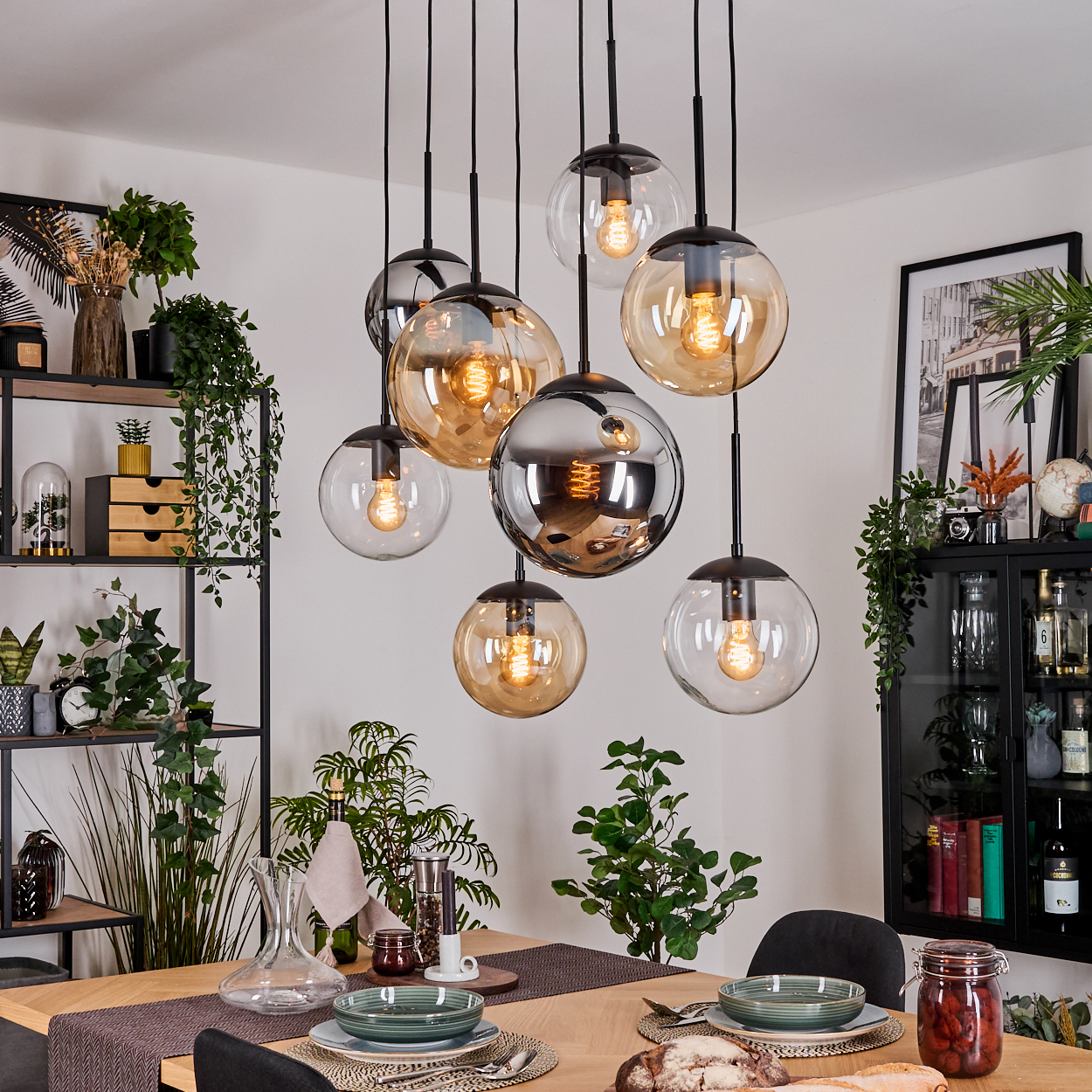 Esszimmer mit hängenden Kugelleuchten. Tisch mit Tellern, Brot. Pflanzen und Regale mit Deko im Hintergrund.