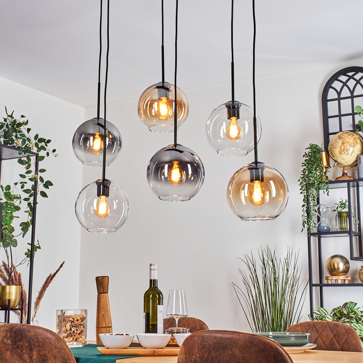 Esszimmer mit sechs hängenden Kugelleuchten. Tisch mit Wein, Schalen und Gläsern. Pflanzen und Regale im Hintergrund.