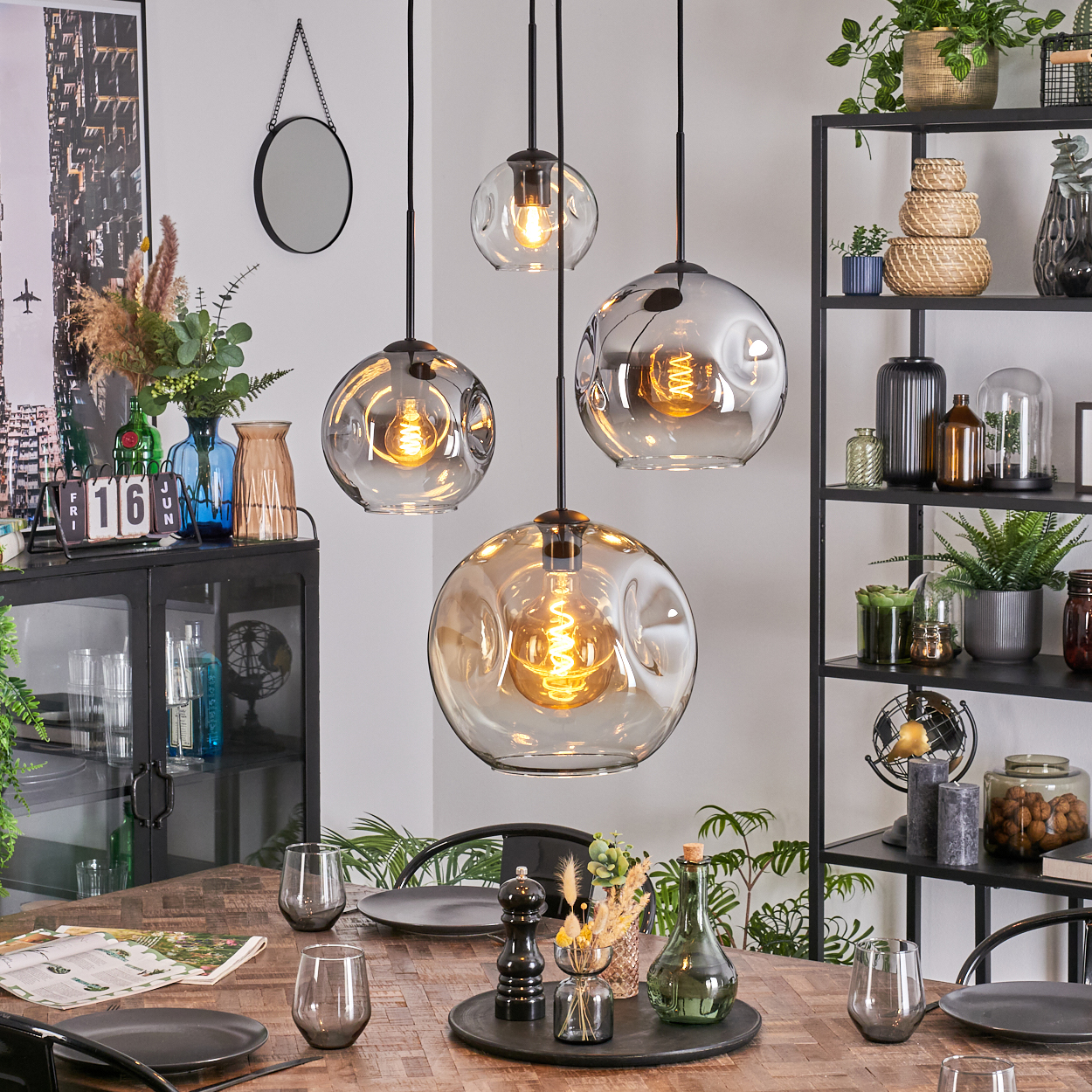 Esszimmer mit Hängelampen, Tisch mit Tellern und Gläsern. Pflanzen und Regale mit Dekor im Hintergrund.
