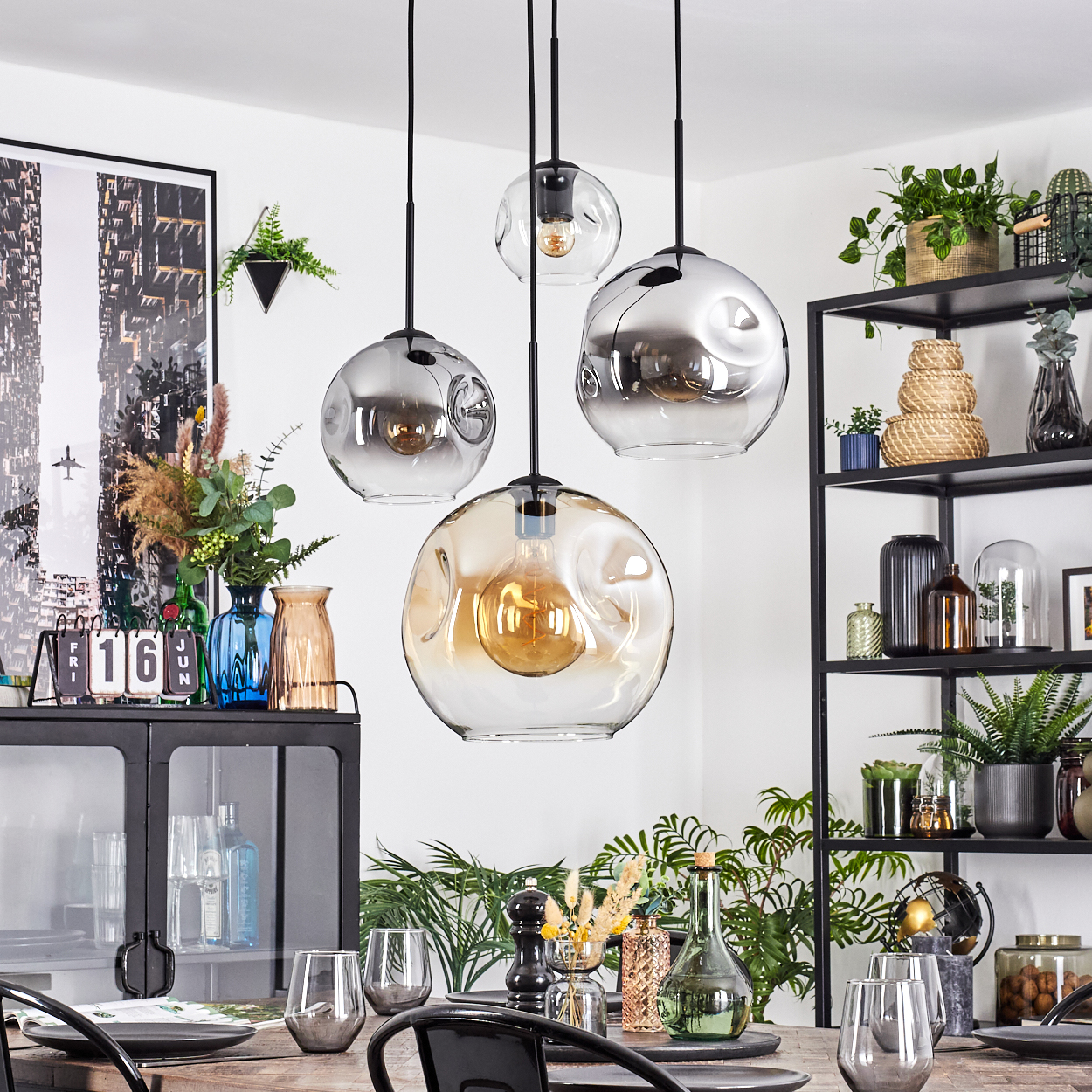 Esszimmer mit hängenden Kugelleuchten, gedecktem Tisch, schwarzem Schrank mit Vasen und einem schwarzen Regal mit Pflanzen und Deko.