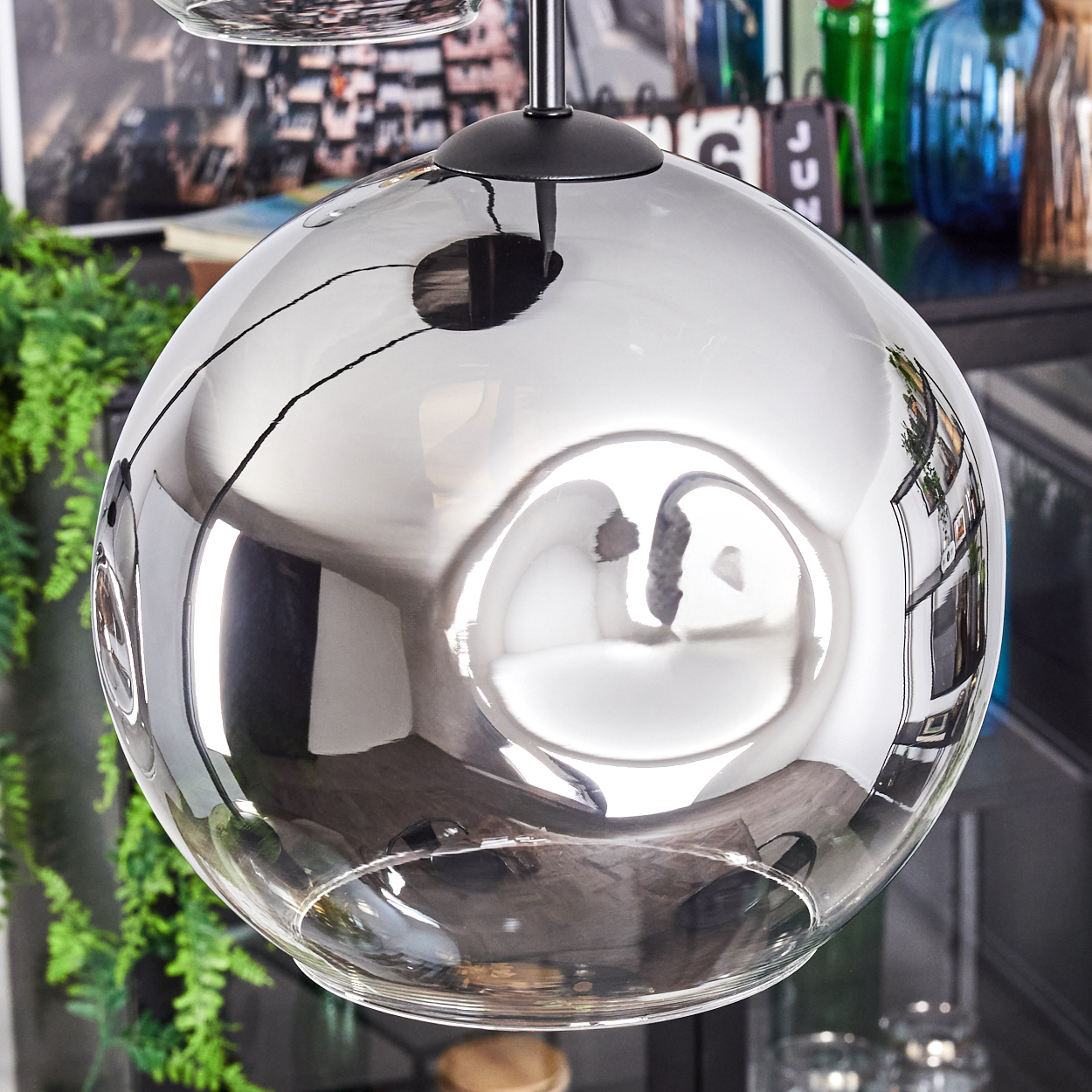 Eine reflektierende, klare Glas-Pendelleuchte. Sie hängt an einer schwarzen Halterung. Die Glaskugel reflektiert den Raum.
