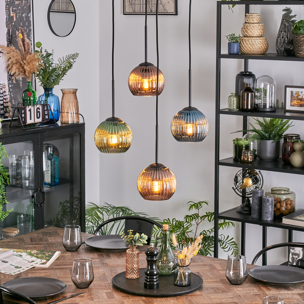 Ein Esszimmer mit Holztisch, Hängelampen und einem schwarzen Regal voller Dekoration. Teller und Gläser sind gedeckt.