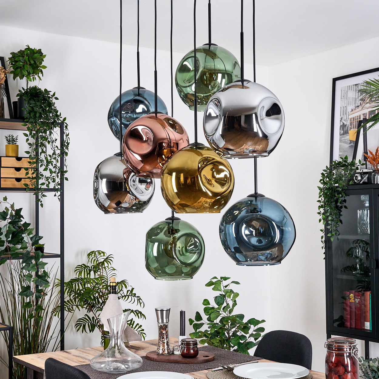 Ein Esszimmer mit hängenden, bunten, kugelförmigen Lichtern. Pflanzen und ein Holztisch sind im Vordergrund. Der Hintergrund umfasst Regale und einen Schrank.