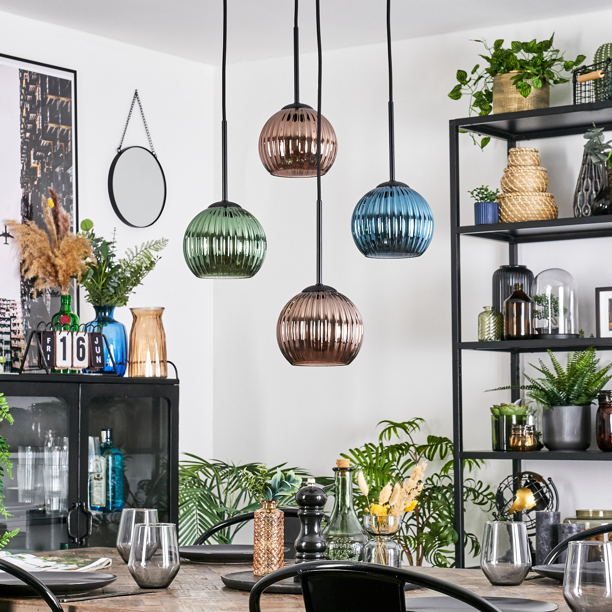 Esszimmer mit Hängelampen, Tischarrangement und Regalen mit Pflanzen und Dekoration. Vier Pendelleuchten hängen über dem Tisch.
