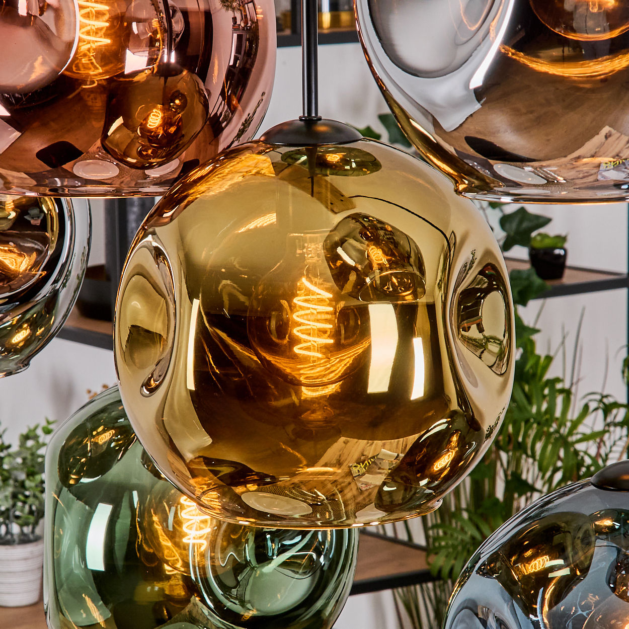 Nahaufnahme von modernen Pendelleuchten mit Glaskugeln in Gold-, Kupfer-, Grün- und Silberfarben. Sichtbare Glühbirnen innen.