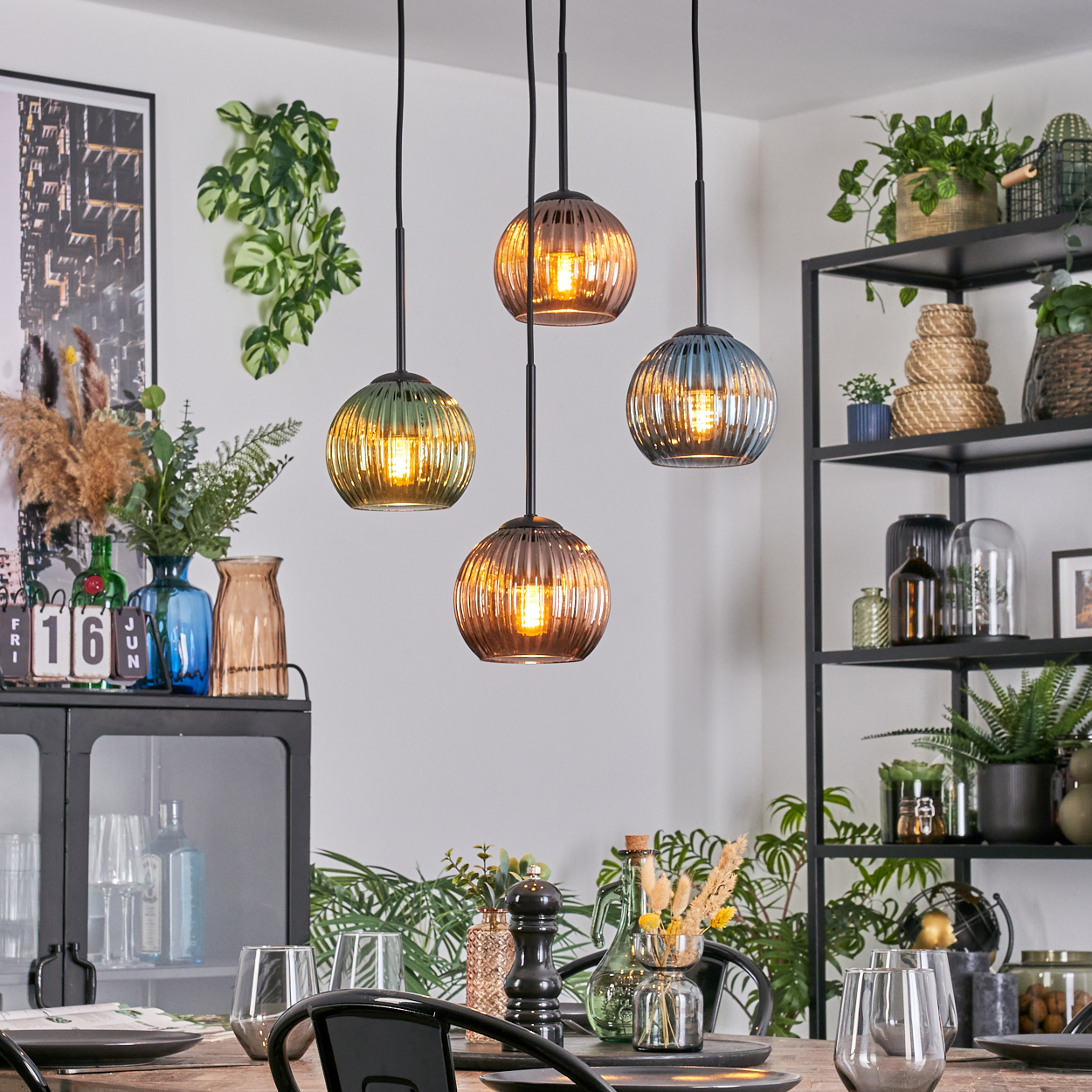 Esszimmer mit hängenden Kugelleuchten. Tisch mit Gläsern und Tellern. Regale mit Pflanzen und Dekoration.
