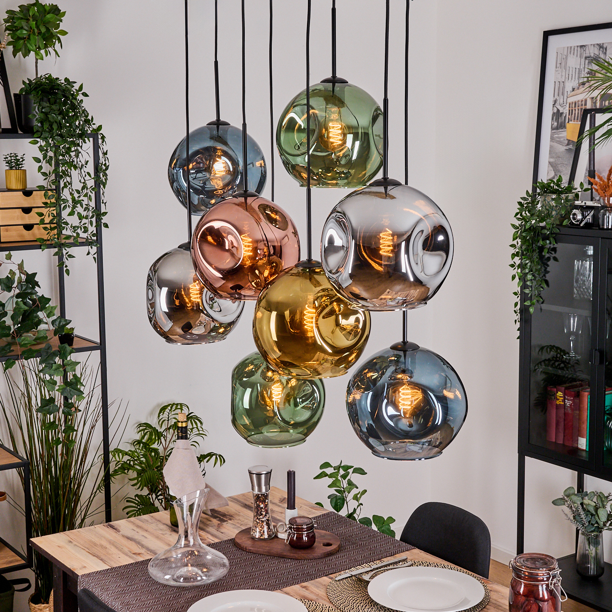 Ein Esszimmer mit Holztisch, hängenden farbigen Glaskugelleuchten, Pflanzen und einem schwarzen Schrank mit Dekoration.