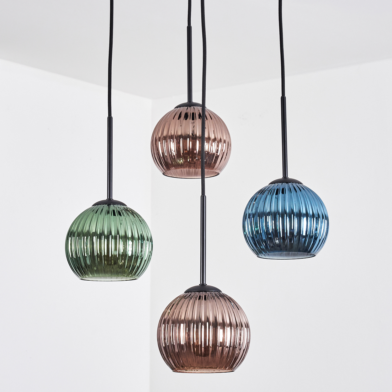 Vier farbige, gerippte Glas-Pendelleuchten hängen an schwarzen Schnüren vor einer weißen Wand. Zu den Farben gehören Grün, Blau und zwei Rosatöne.