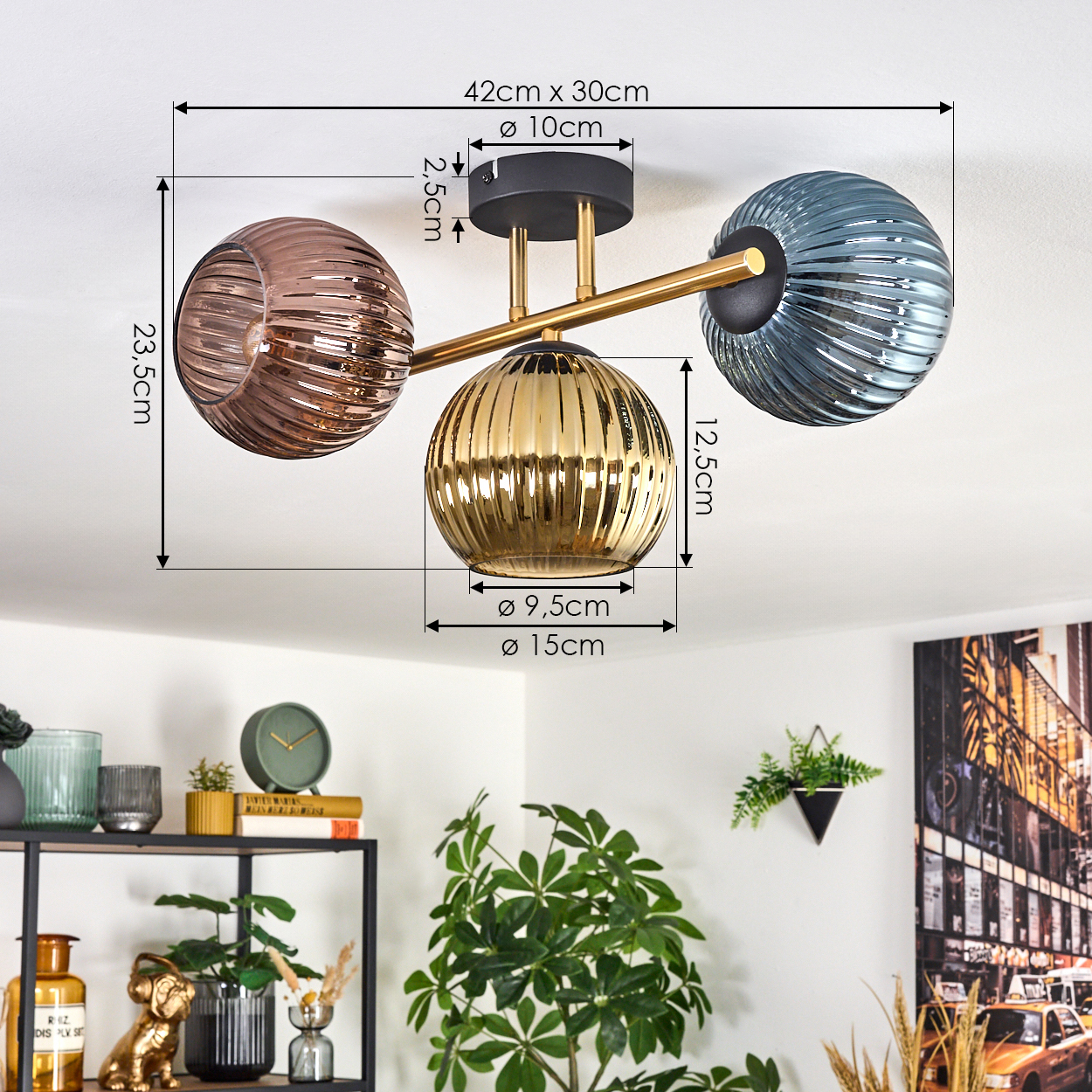 Eine moderne Deckenlampe mit drei kugelförmigen Lampenschirmen: braun, gold und blau. Im Vordergrund ein Regal mit Dekor und Pflanzen.