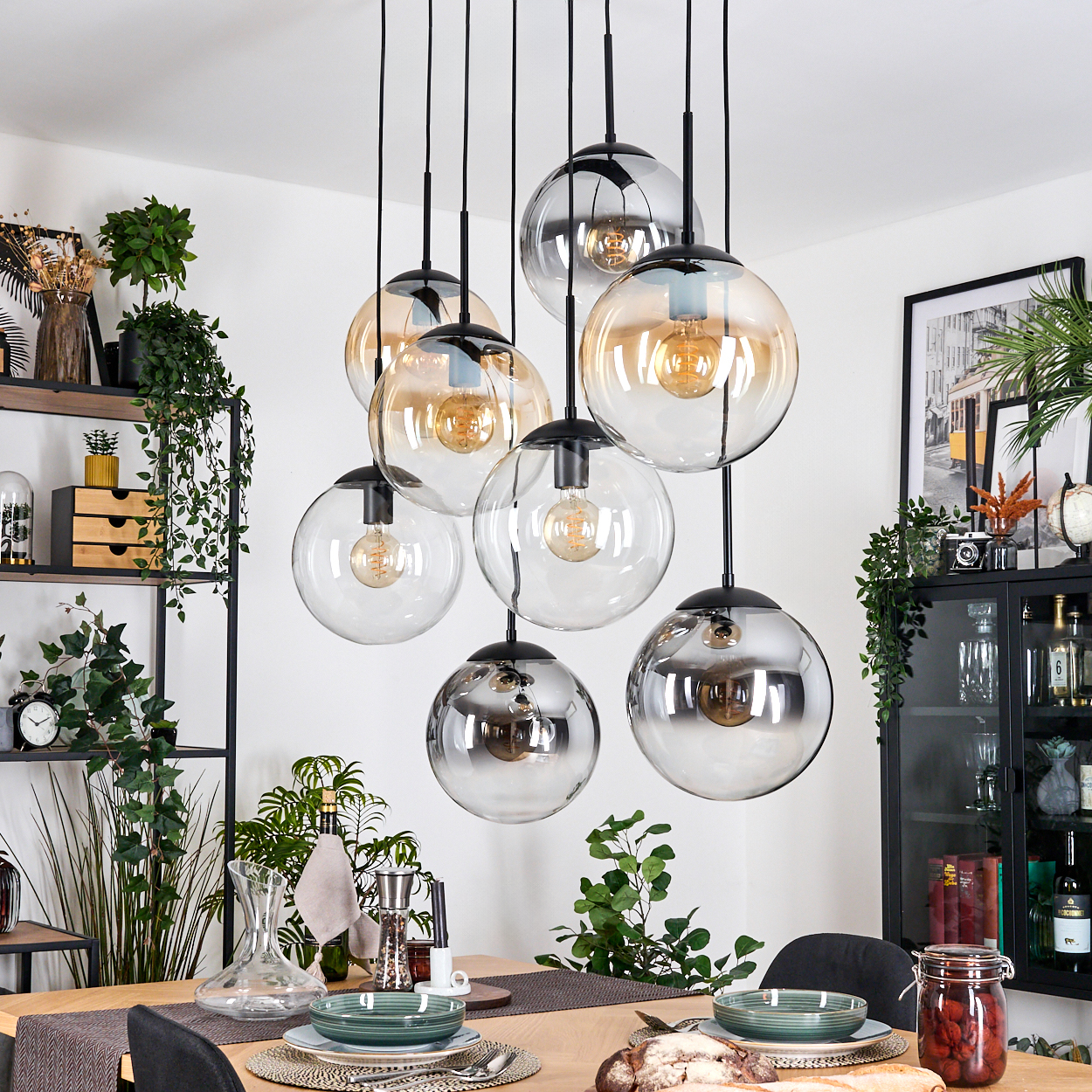 Esszimmer mit Hänge-Kugelleuchten. Tisch mit Tellern und Dekoration. Grüne Pflanzen im Hintergrund.