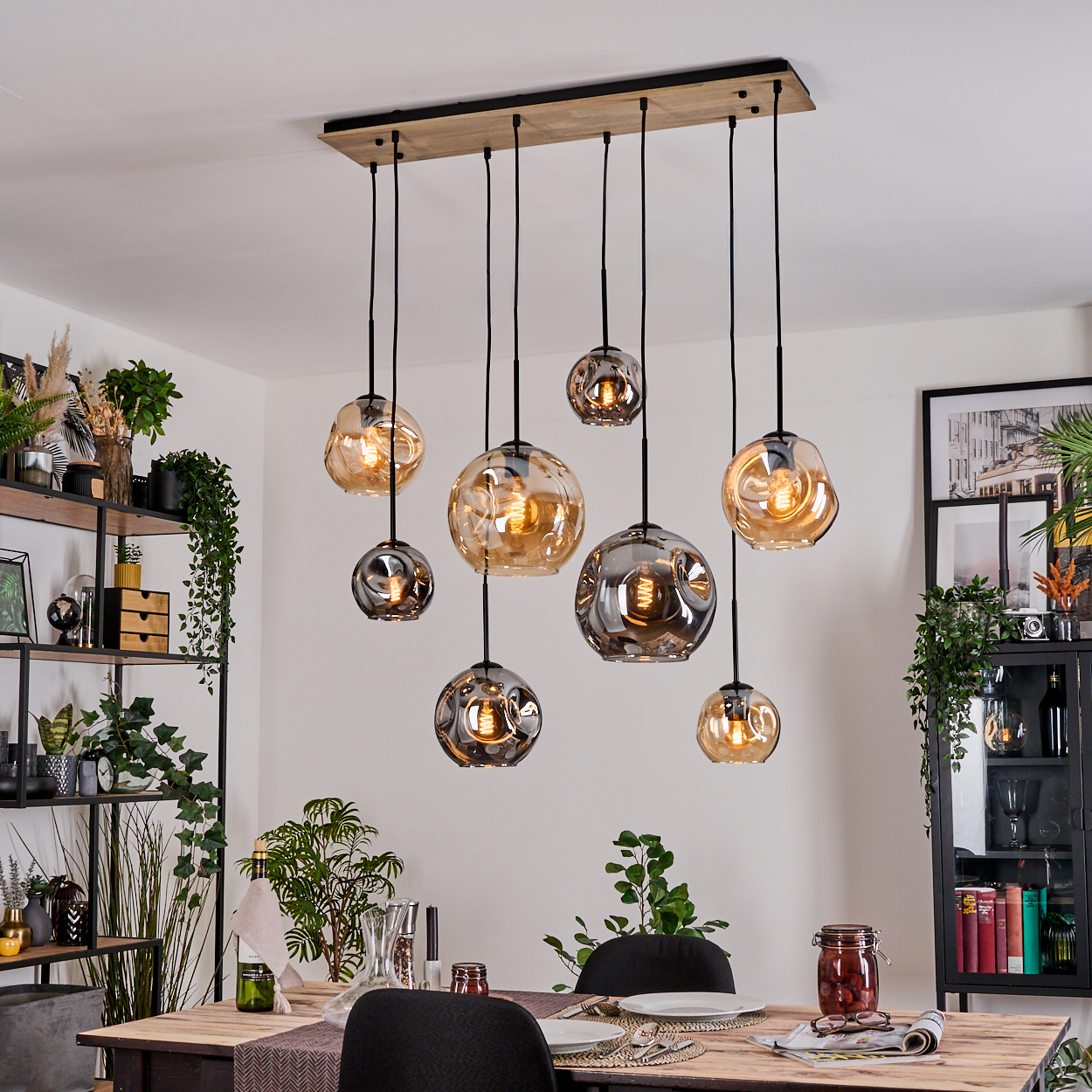Esszimmer mit Holztisch, Stühlen und einzigartiger Hängelampe mit kugelförmigen Lichtern. Pflanzen und Dekorationen sind sichtbar.
