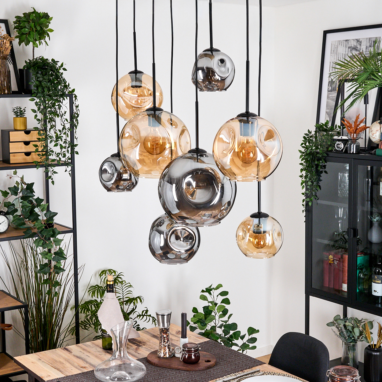 Esszimmer mit hängenden Glaskugelleuchten. Ein Holztisch ist mit Dekoration gedeckt. Pflanzen und Regale sind im Hintergrund.