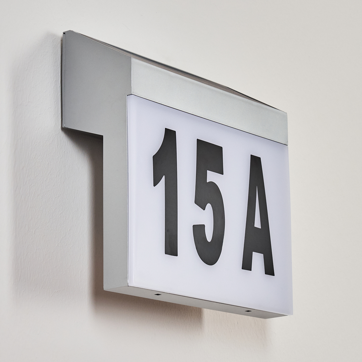 Ein beleuchtetes Schild mit der Aufschrift 15A auf einer weißen Oberfläche. Das Schild hat einen silbernen Rahmen und ist an einer weißen Wand befestigt.