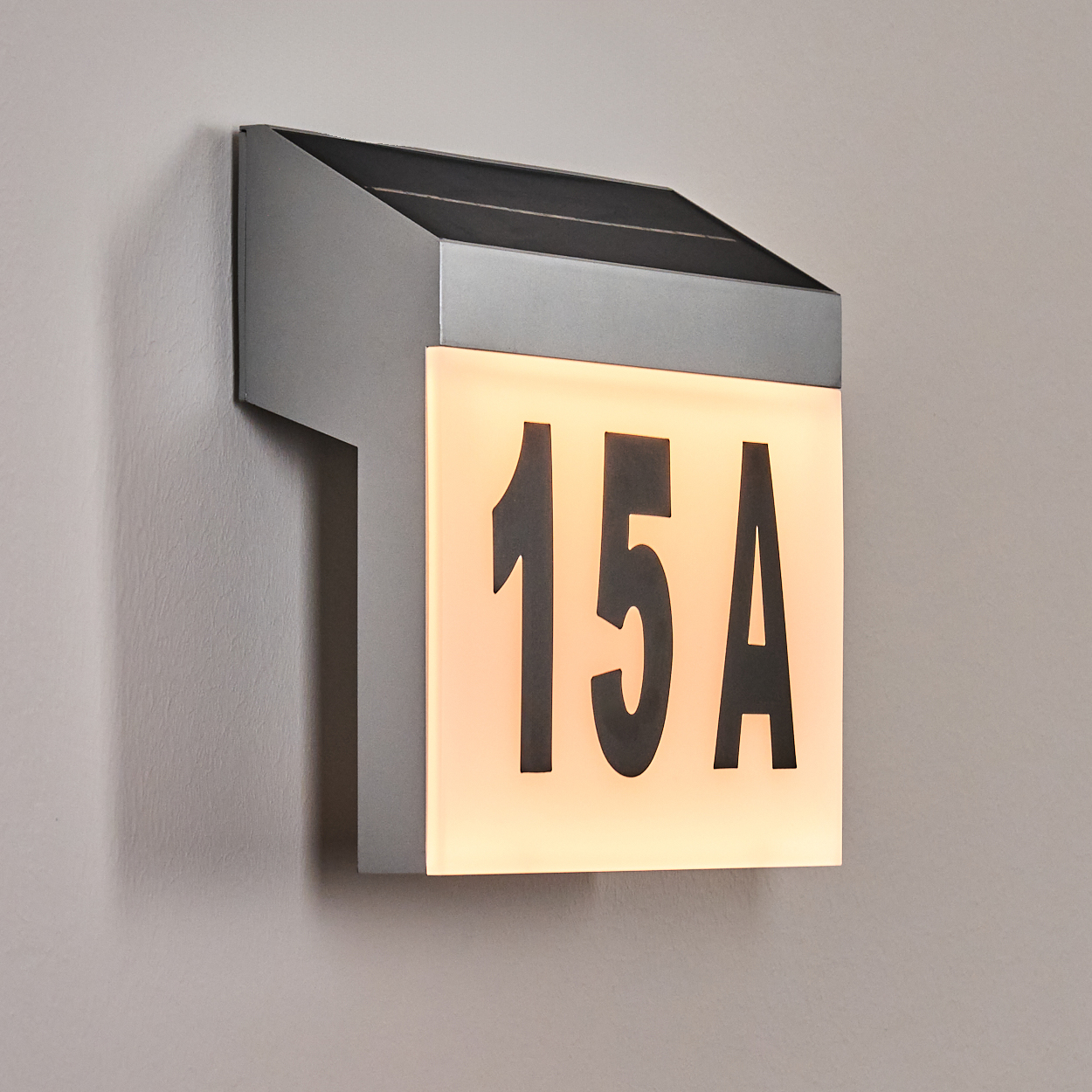 Ein modernes, beleuchtetes Hausnummernschild. Es zeigt die Nummer "15A" in Schwarz auf orangefarbenem Hintergrund.