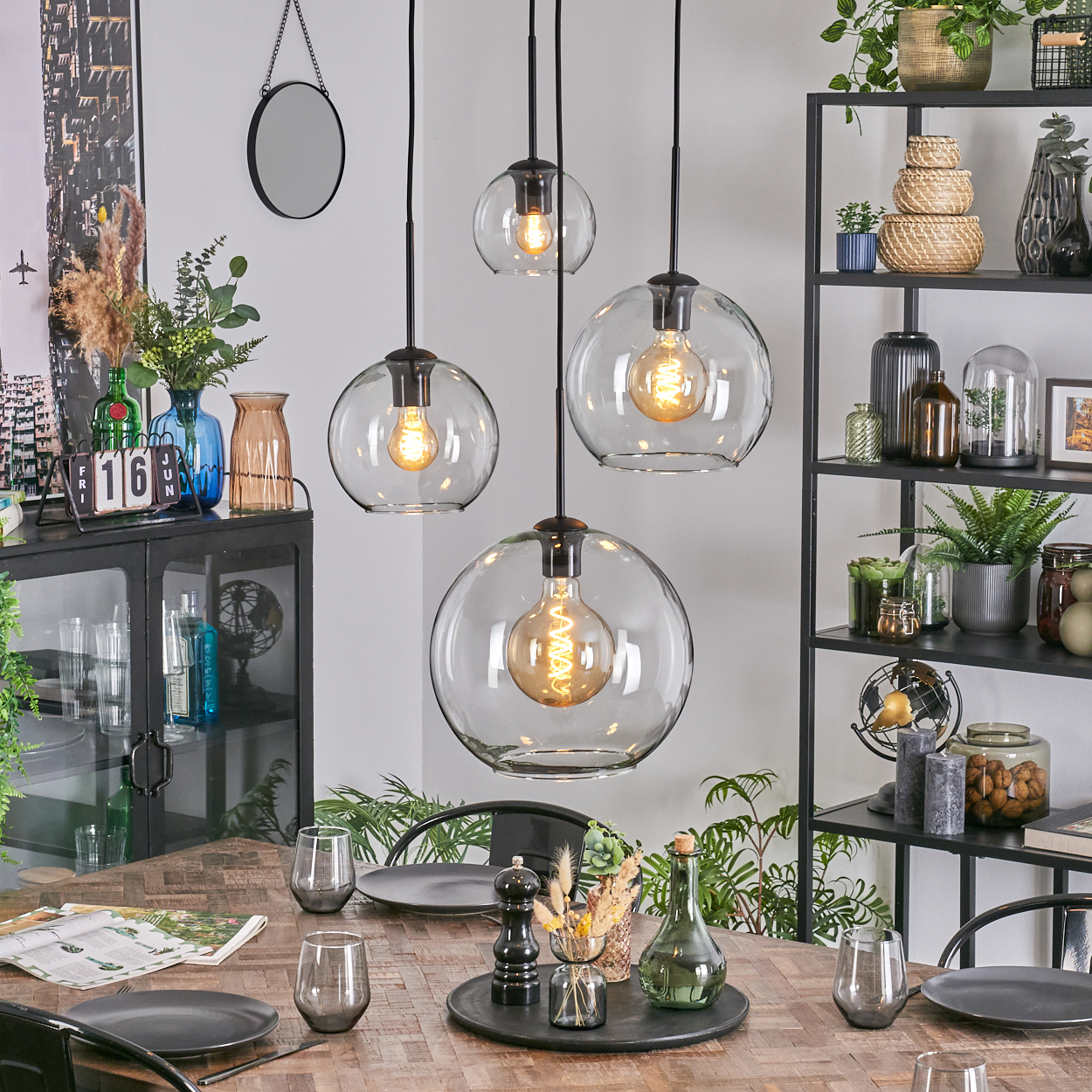Esszimmer mit Hängeleuchten, Tisch mit Tellern und Gläsern, Regale mit Pflanzen und Dekor.